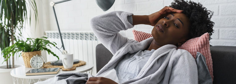 visibily sick woman in a bath robe surrounded by tissues suffers ailment reclined in a chair