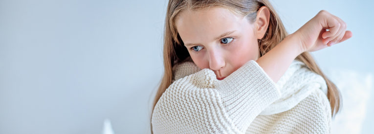 Girl in white sweater coughs into elbow