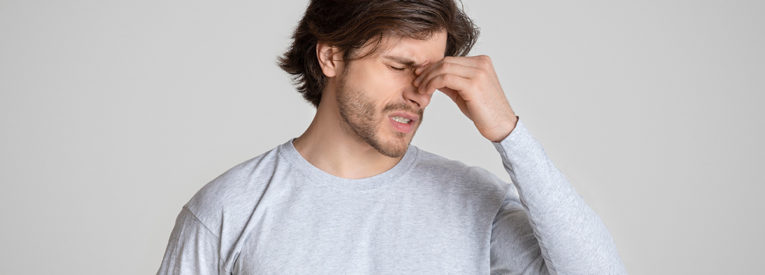 man holds the bridge of his nose in obvious pain